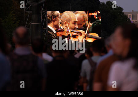 Berlin, Germany. 24th Aug, 2019. On a screen on Straße des 17. Juni people follow the concert of the Berliner Philharmoniker under the direction of the new chief conductor Kirill Petrenko. Credit: Paul Zinken/dpa/Alamy Live News Stock Photo