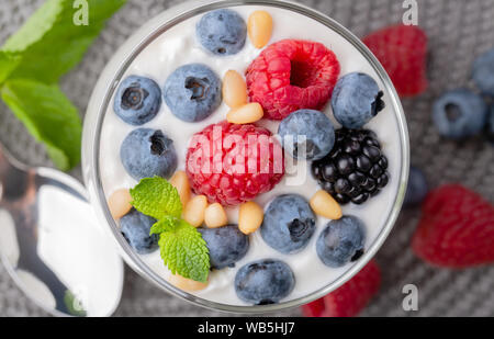 A glass of granola in yogurt with a mix of wild berries on a gray table. Top view, macro shot Stock Photo