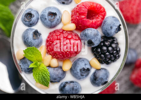 A glass of granola in yogurt with a mix of wild berries on a gray table. Top view, macro shot Stock Photo