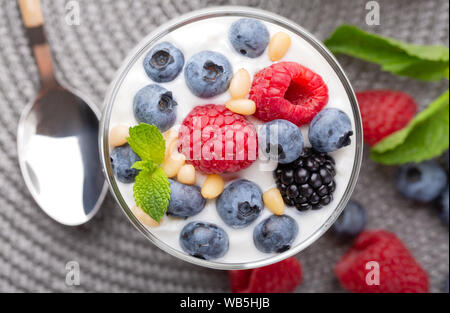 A glass of granola in yogurt with a mix of wild berries on a gray table. Top view, macro shot Stock Photo