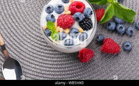 A glass of granola in yogurt with a mix of wild berries on a gray table. Top view, macro shot Stock Photo