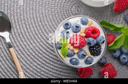 A glass of granola in yogurt with a mix of wild berries on a gray table. Top view, macro shot Stock Photo