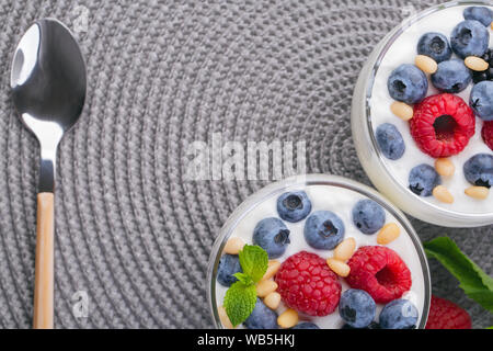 A glass of granola in yogurt with a mix of wild berries on a gray table. Top view, macro shot Stock Photo