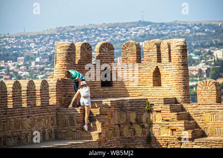 Man reaches down to give girl a hand climbing up steps in Narikala Castle in Old Town with Tbilisi Georgia blurred out in the distance Stock Photo