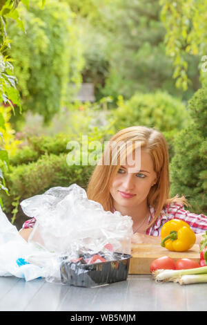 Young woman is showing how much plastic packaging remains after unpacking vegetables bought in a  store. Vertically. Stock Photo