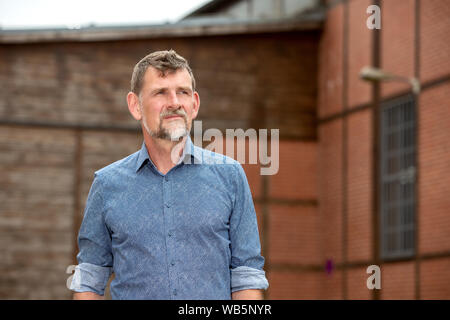 portrait of handsome man in his 50s in blue shirt standing outside Stock Photo