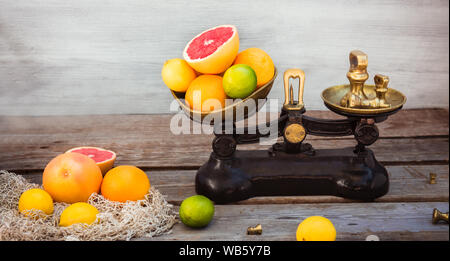 Fresh citrus fruits on the one scalepan of vintage weights and and few oranges, lemons, grapefruit, lime on the rustic wooden table. Detox diet. Harve Stock Photo