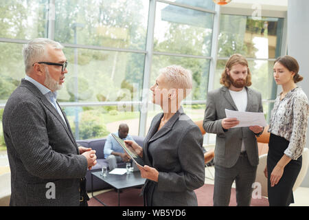 Portrait of diverse group of business people working in hall of modern office building focus on two senior managers in foreground, copy space Stock Photo