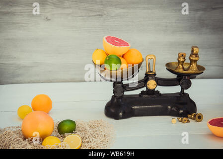 Fresh citrus fruits on the one scalepan of vintage weights and several oranges, lemons, grapefruit, lime on the white wooden table. Detox diet. Harves Stock Photo