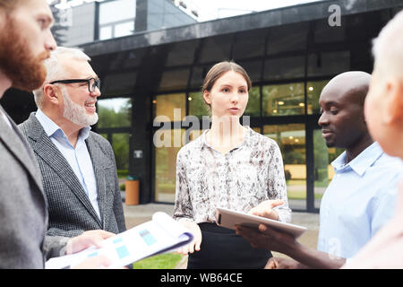 Portrait of diverse group of business people discussing work standing outdoors, focus on young woman in center Stock Photo