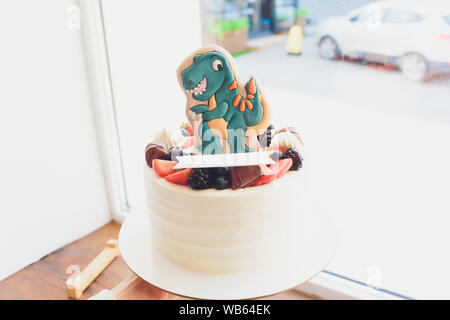 Children's holiday white cake decorated with mastic figurines of dinosaurs in the Jurassic period jungle. Concept ideas desserts for kids Stock Photo