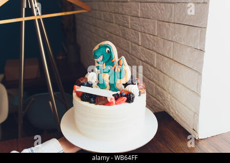 Children's holiday white cake decorated with mastic figurines of dinosaurs in the Jurassic period jungle. Concept ideas desserts for kids Stock Photo