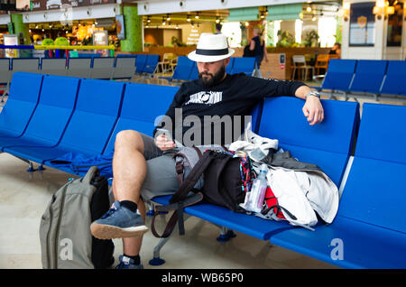 Young man with hat using a smartphone while is waiting with his luggage in an airport Stock Photo