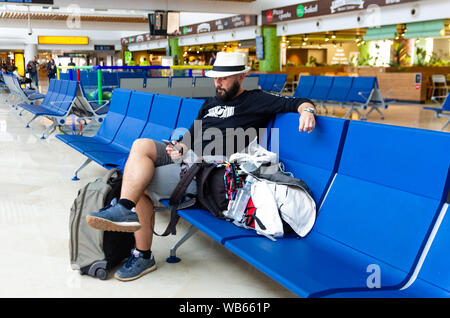 Young man with hat using a smartphone while is waiting with his luggage in an airport Stock Photo