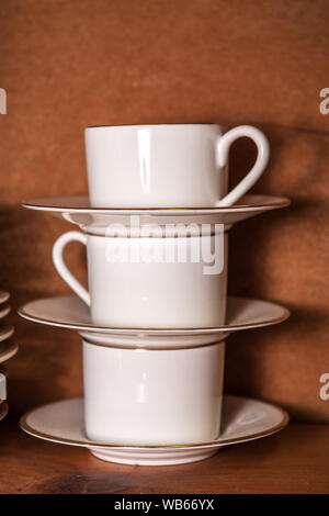 stack of porcelain coffee cups with gold rim on wooden background Stock Photo