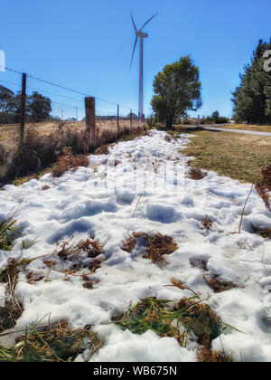 Wind turbine on an agriculture farm in Australian Blue MOuntains during winter season when white snow falls to green grass high on plateau along the r Stock Photo
