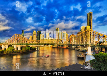 Small passenger ferry on still waters of Brisbane river in Brisbane city CBD under Story bridge lit by soft morning sky. Stock Photo