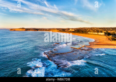 Yellow sand beach of Mona Vale suburb on Sydney Northern Beaches with rock pool outstanding on a tip of sandstone plateau in Pacific ocean - aerial vi Stock Photo