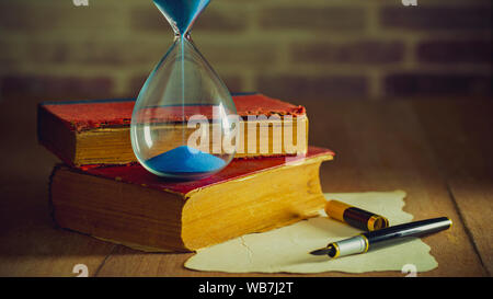 Sand clock with old books and pen with paper map on the wooden table. Concept of travel planning. Stock Photo