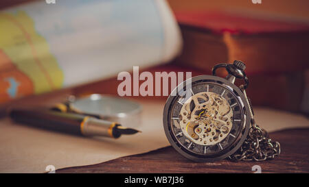 Pocket watch with old books and pen with paper map on the table by the window. Concept of travel planning. Stock Photo