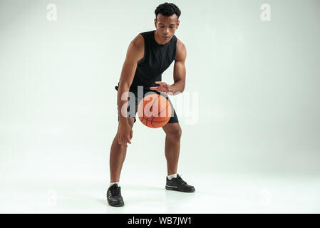 Real player. Full length of young african man in sports clothing playing basketball in studio against grey background. Active lifestyle. Professional sport Stock Photo