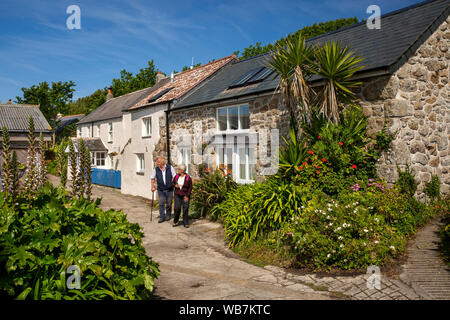 UK, England, Scilly Islands, St Martin’s, Middle Town, senior tourist couple walking on main road, past stone cottages Stock Photo