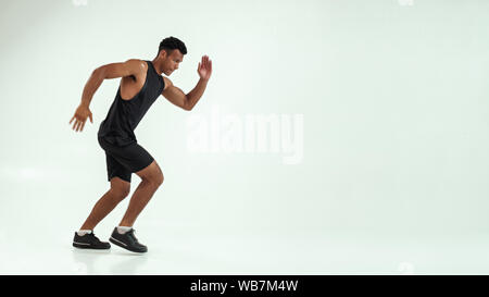 Full length of young african man with muscular body in sports clothing preparing to run in studio against grey background. Sport concept. Motivation. Healthy lifestyle Stock Photo
