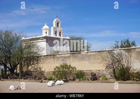 The historic San Xavier Mission, located near Tucson, Arizona, can be seen beyond a dirty adobe wall under a bright blue sky on a sunny spring day Stock Photo