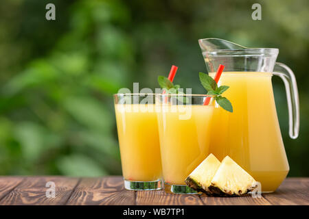 fresh pineapple juice in two glasses and jug on wooden table outdoors. Summer refreshing drink Stock Photo