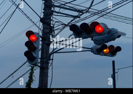 Silhouette of four traffic lights hanging from the same post and electricity cables at dusk in Japan. Stock Photo