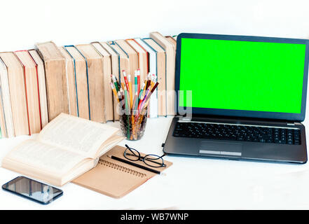 Green screen laptop, pile if books, notebook, smartphone, glasses and pencils in holder on white table, education concept background Stock Photo