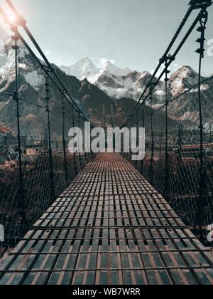Vertical shot of a bridge with a metal fence and snowy mountains in the background Stock Photo