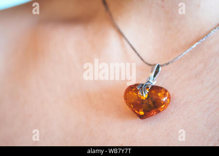 A heart shaped amber pendant worn around the neck of a young woman Stock Photo