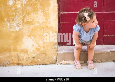 Cute baby girl sitting on the doorstep of a rural village home Stock Photo