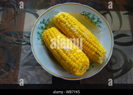 Tasty yellow boiled Ukrainian two pumpkins of corn and salt laid out on plates with green flowers. Stock Photo