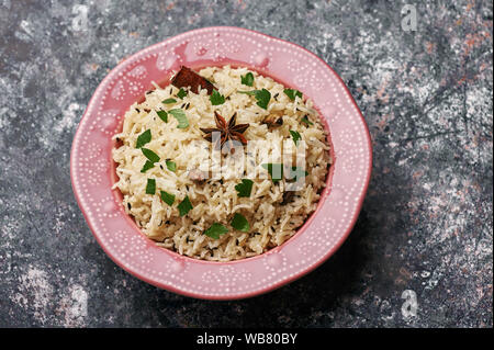 Jeera Rice in pink plate at dark bacgkround. Jeera rice - traditional indian cuisine dish with basmati rice, cumin, coriander, star anise and cardamon Stock Photo
