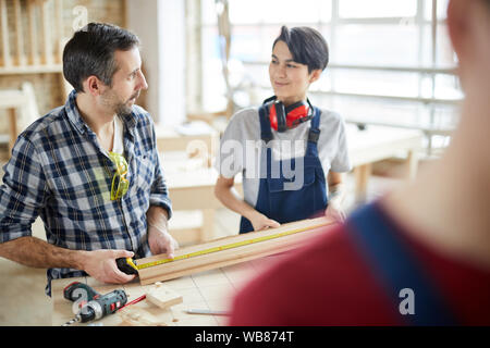 Waist up portrait of mature carpenter working to smiling female apprentice in workshop, copy space Stock Photo