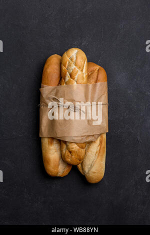 Tree loafs of bread in craft paper at black background. Concept of banner for market Stock Photo