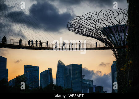 Sunset view of famous landmarks of Singapore with suspension bridge and tourist over skyscrapers of Marina Bay Financial Center and futuristic tree Stock Photo