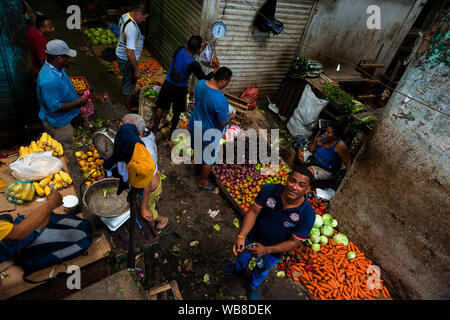 Afro-Colombian men walk along piles of fruits and vegetables while shopping in the market of Bazurto in Cartagena, Colombia. Stock Photo