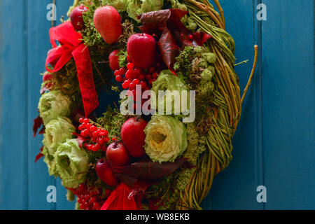 Wreath with red apples, berries and roses hanging on a blue door. Stock Photo