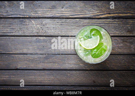 Refreshing mint cocktail mojito with rum and lime, cold drink or beverage with ice on dark wooden background, top view Stock Photo