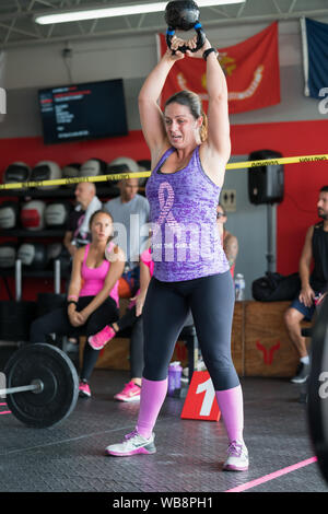 A mixed race woman is doing kettle bell exercises at her gy, with people watching Stock Photo