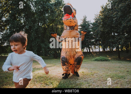 Father and son playing at the park, with a dinosaur costume, having fun with the family outdoor Stock Photo