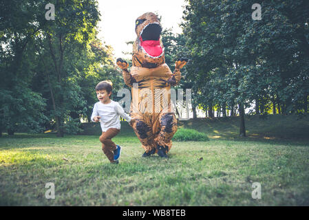 Father and son playing at the park, with a dinosaur costume, having fun with the family outdoor Stock Photo