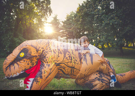Father and son playing at the park, with a dinosaur costume, having fun with the family outdoor Stock Photo