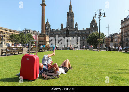 Glasgow, Scotland, UK. 25 August 2019. As temperatures soar to over 26C in Glasgow after days of rain and cold wind, people flock to the city's open spaces of George Square and the Botanic Gardens to take advantage of late summer sun on this August Bank Holiday, to top up their tans and relax. Credit: Findlay/Alamy Live News