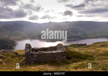 A derelict stone hut on the Old Corpse Road above Haweswater Reservoir in the English Lake District. In the far distance is Kidsty Pike & High Street Stock Photo