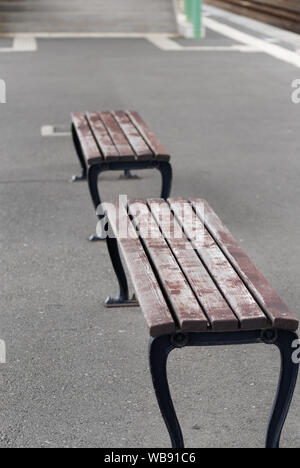 Black and white image of two empty old wooden benches on a train platform. Stock Photo