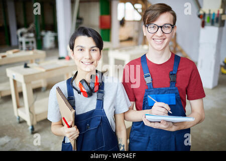 Waist up portrait of two young workers smiling cheerfully at camera while standing in carpentry workshop, copy space Stock Photo